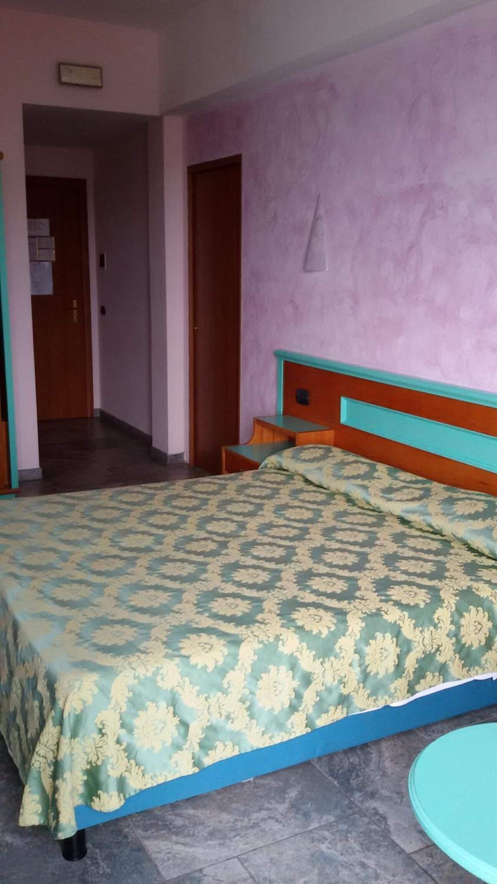 A bedroom with a bed, a nightstand, a door, and a small round table.