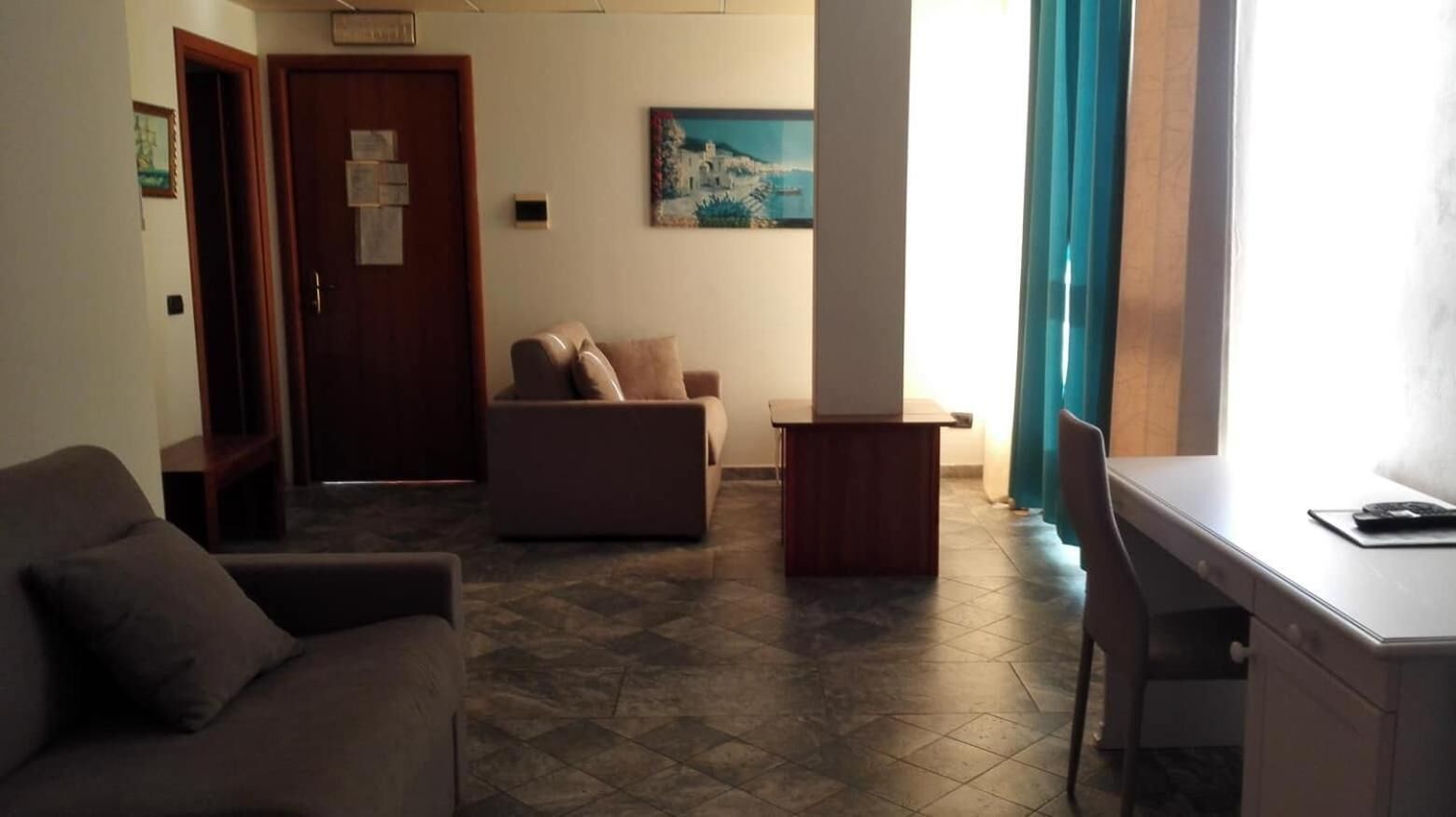 Ein Wohnzimmer mit einer Couch, einem kleinen Tisch und einem Schreibtisch. Eine Tür und ein Gemälde sind an der Wand zu sehen.