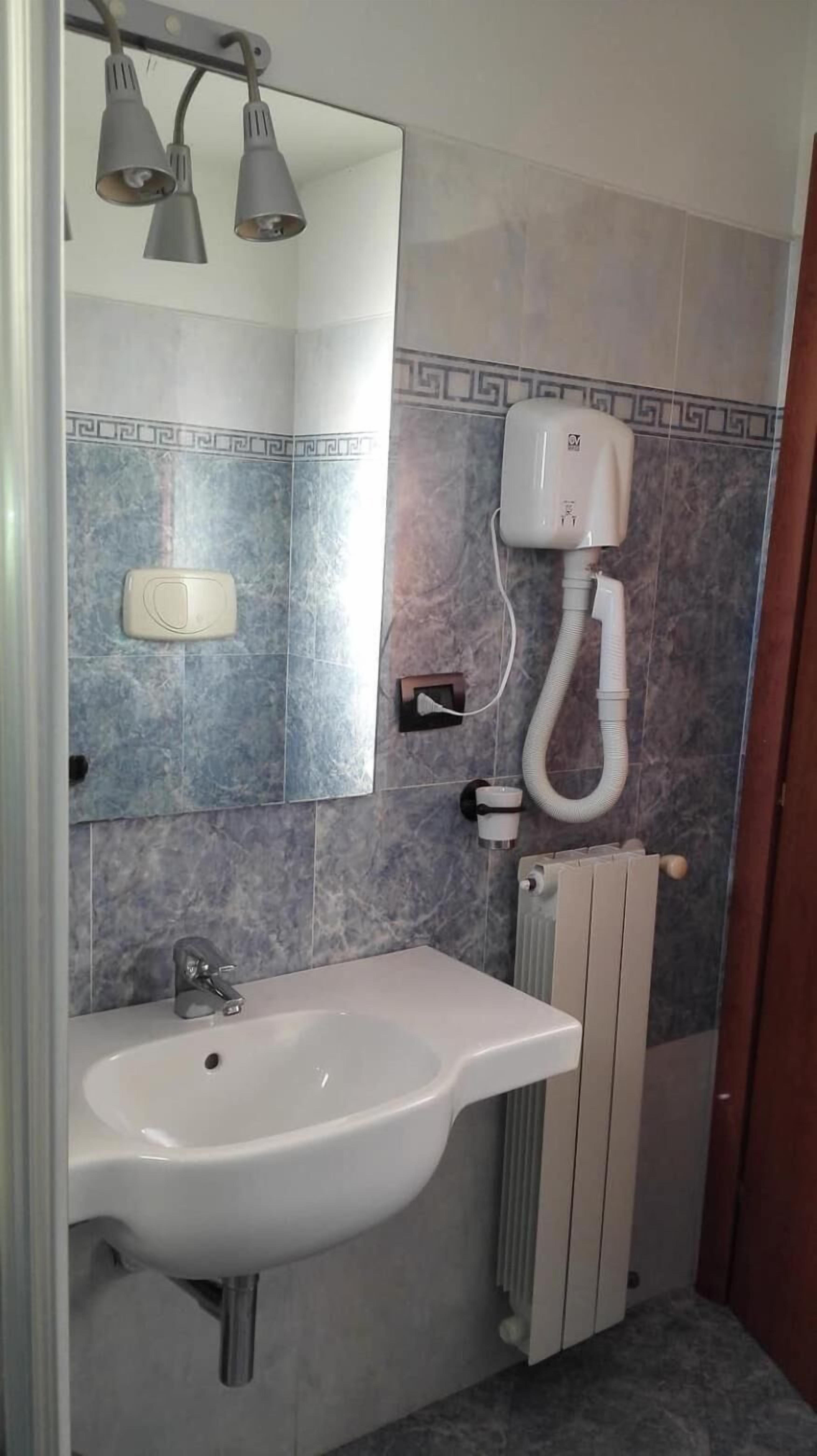 Un baño con lavamanos blanco, un espejo, toallero, calentador y sistema de ventilación.