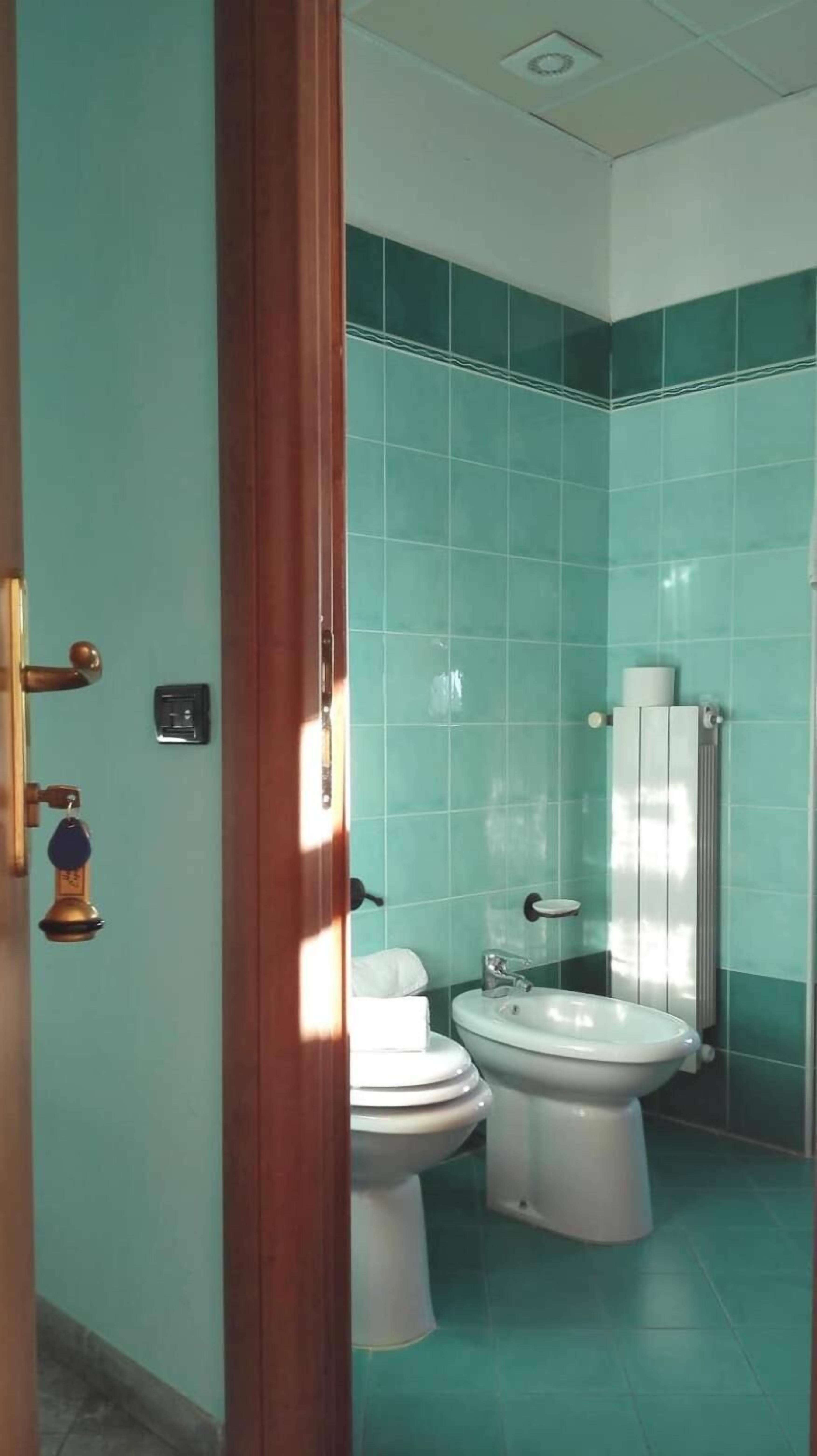 A bathroom with teal tiles, a white toilet, a bidet, and a sink.