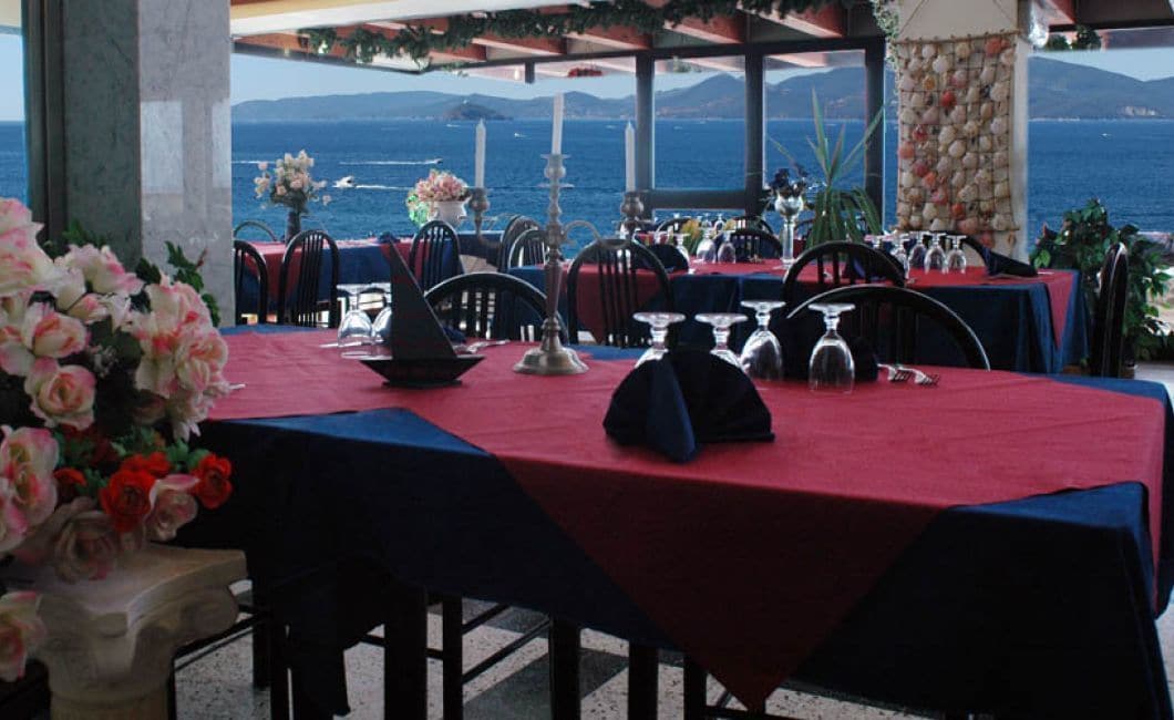An outdoor dining area with tables set for two, overlooking a scenic ocean view.