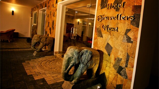 A hotel lobby with a stone wall, a large elephant sculpture, and a sign reading "Hotel Travellers West". - Hotel Travellers Nest (Kandy)