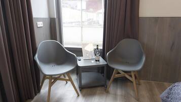 A room with two grey chairs, a small table with a bottle and a glass, and a window with curtains.