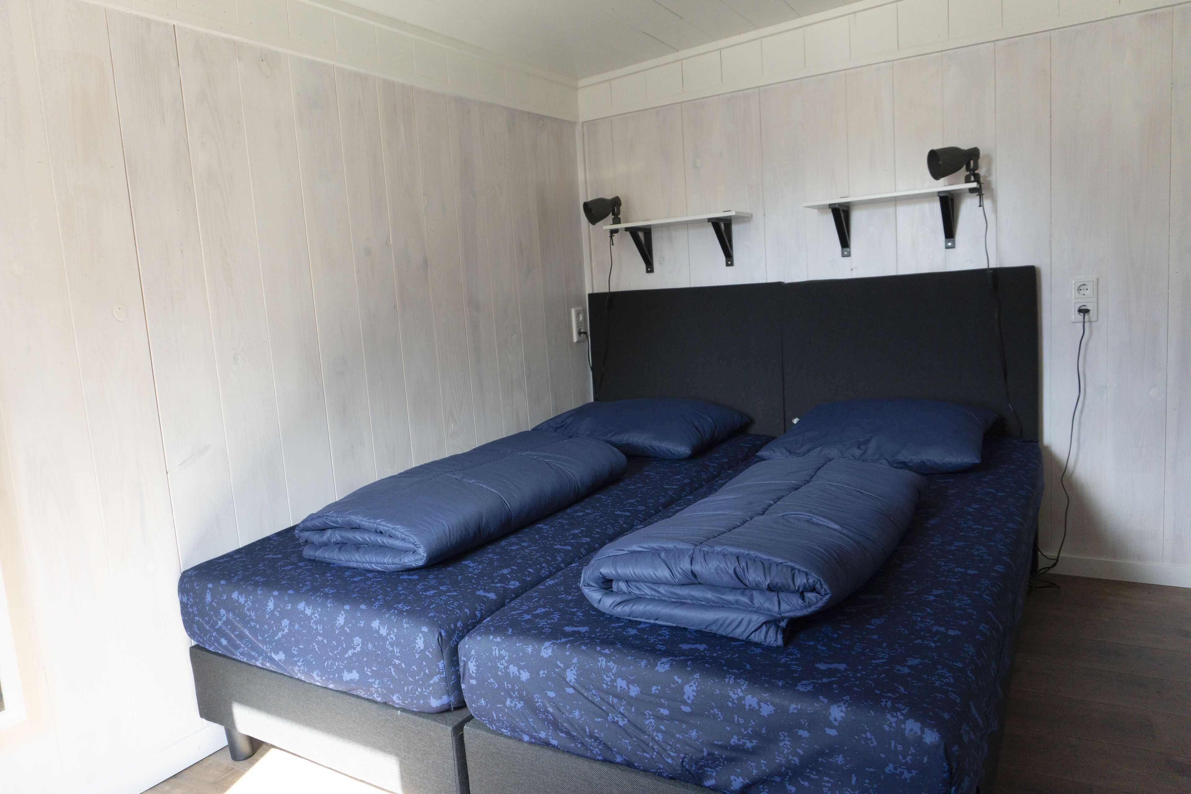 Un lit double avec une tête de lit sombre et un mur de couleur claire.