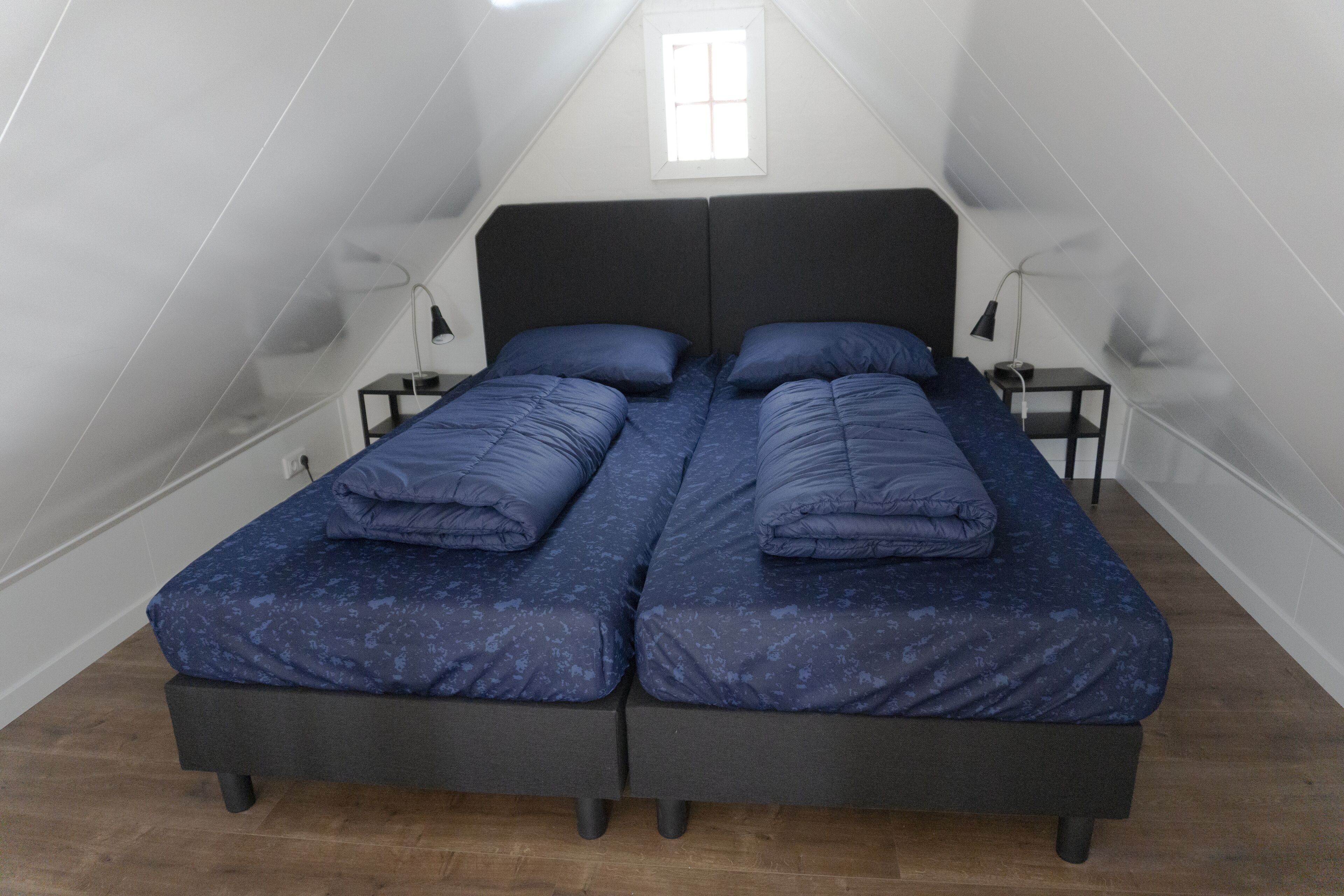 A twin bed room with a sloped ceiling and a window.