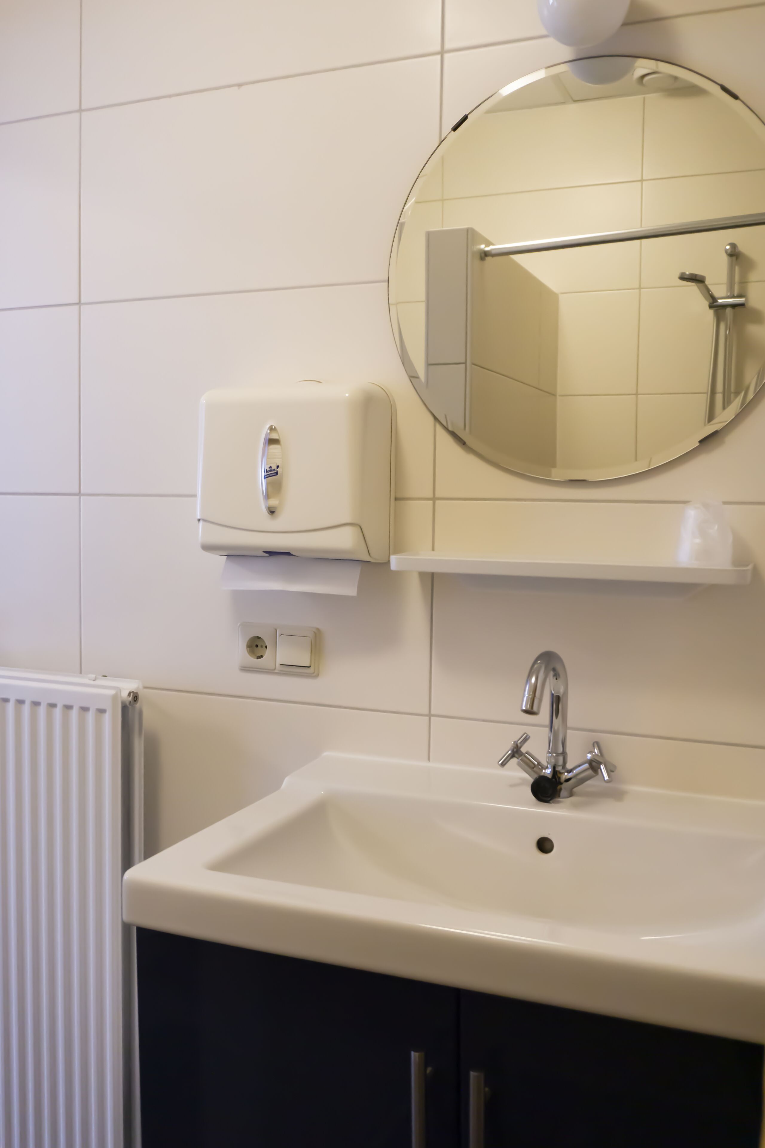 A bathroom with a white sink, a mirror, a towel dispenser, and a toilet paper holder.