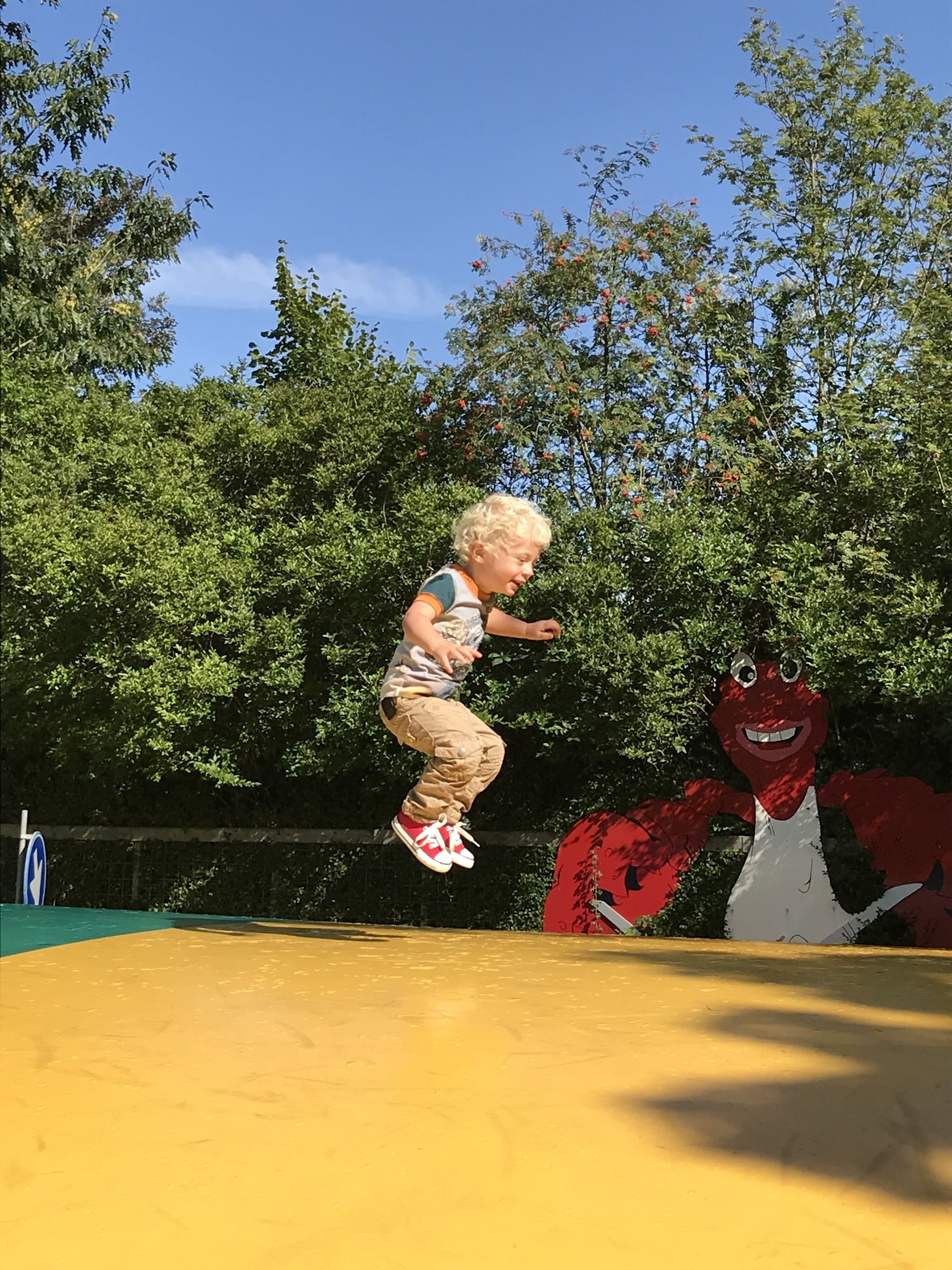 Un niño saltando en un trampolín, con un personaje de dibujos animados rojo al fondo.
