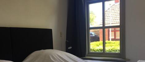Une chambre d’hôtel avec deux lits, une grande fenêtre avec des rideaux et une vue sur un immeuble et de la verdure.