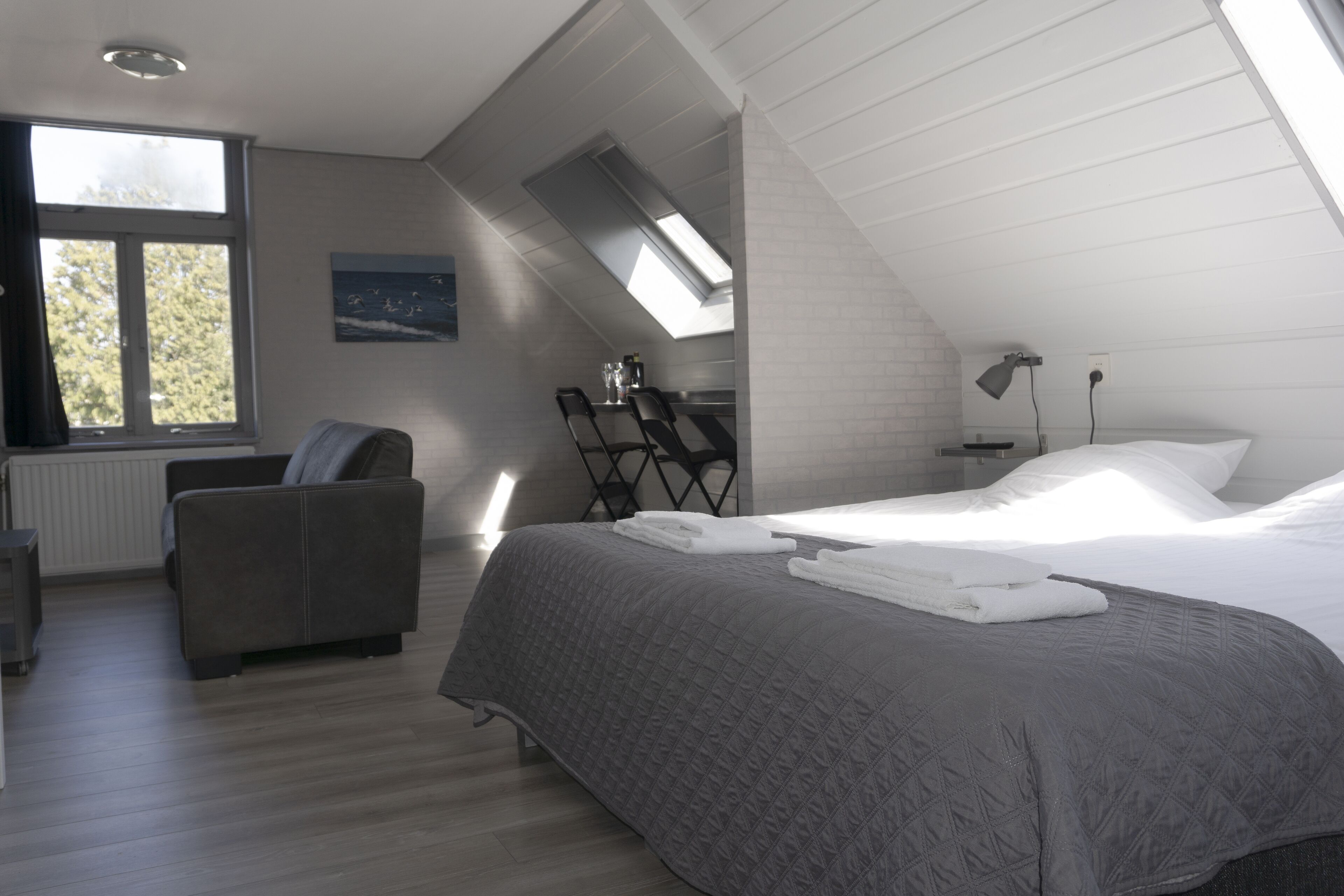 Un dormitorio moderno con una cama grande, una silla, un escritorio y un tragaluz.