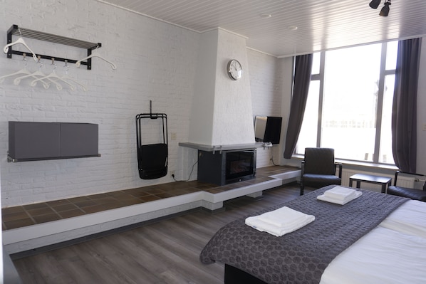 Habitación de hotel con chimenea, una cama, una silla, un televisor y un ventanal con cortinas.