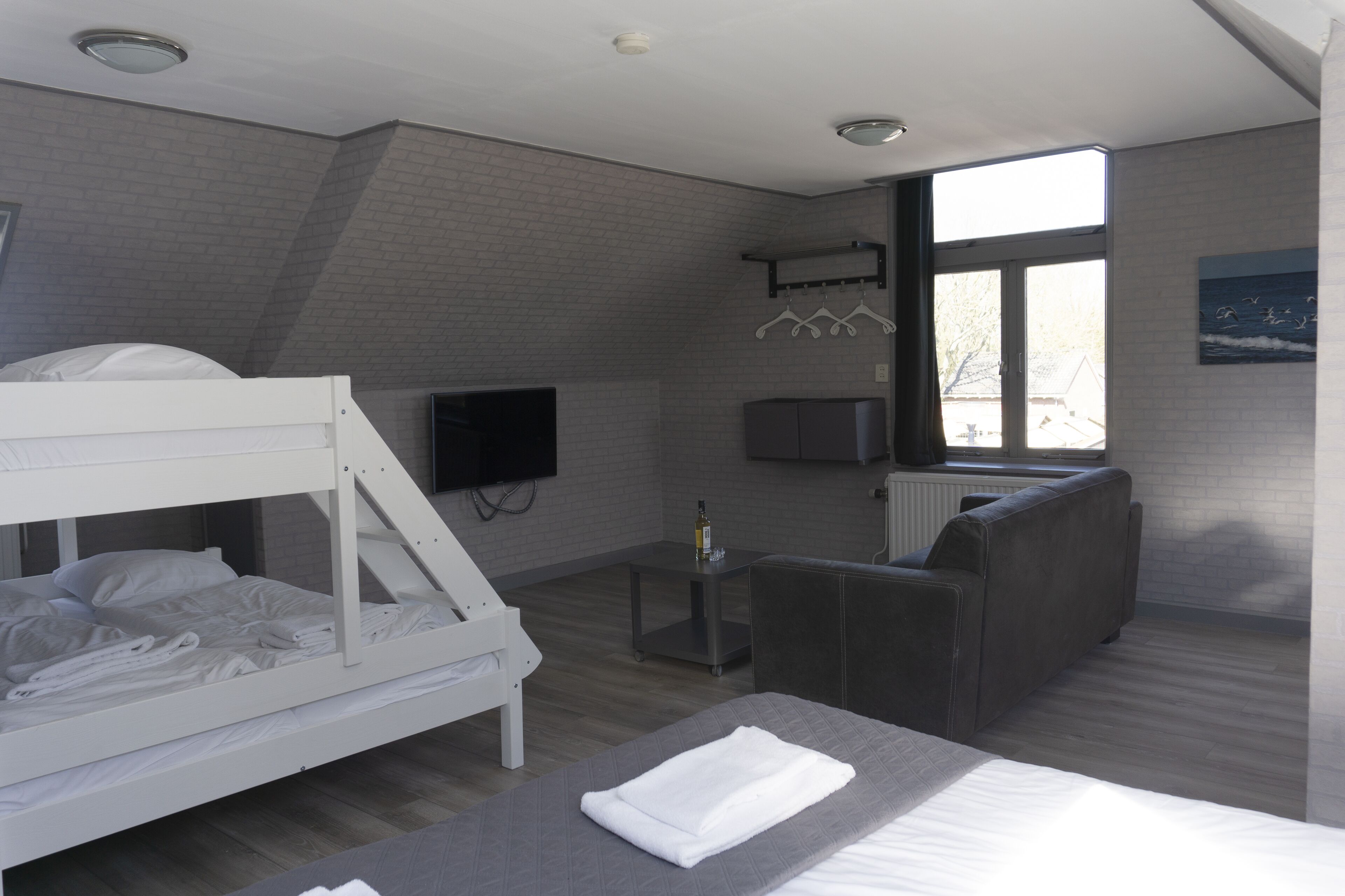 A modern hotel room with a bunk bed, a sofa, a TV, and a window with a view.