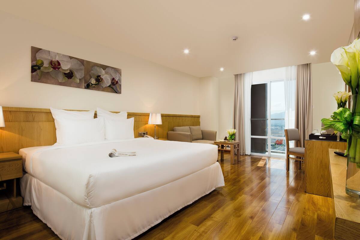 Een hotelkamer met een groot bed, een bureau, een stoel en uitzicht op de stad.