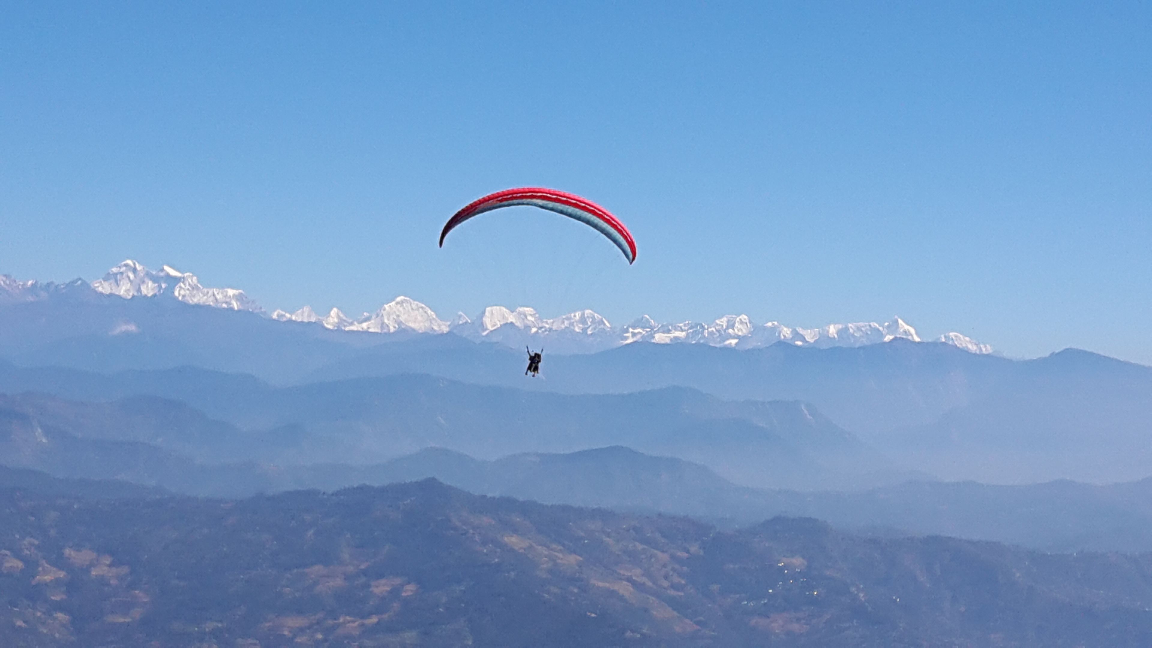 A person paragliding over a mountainous landscape with snow-capped peaks in the background.