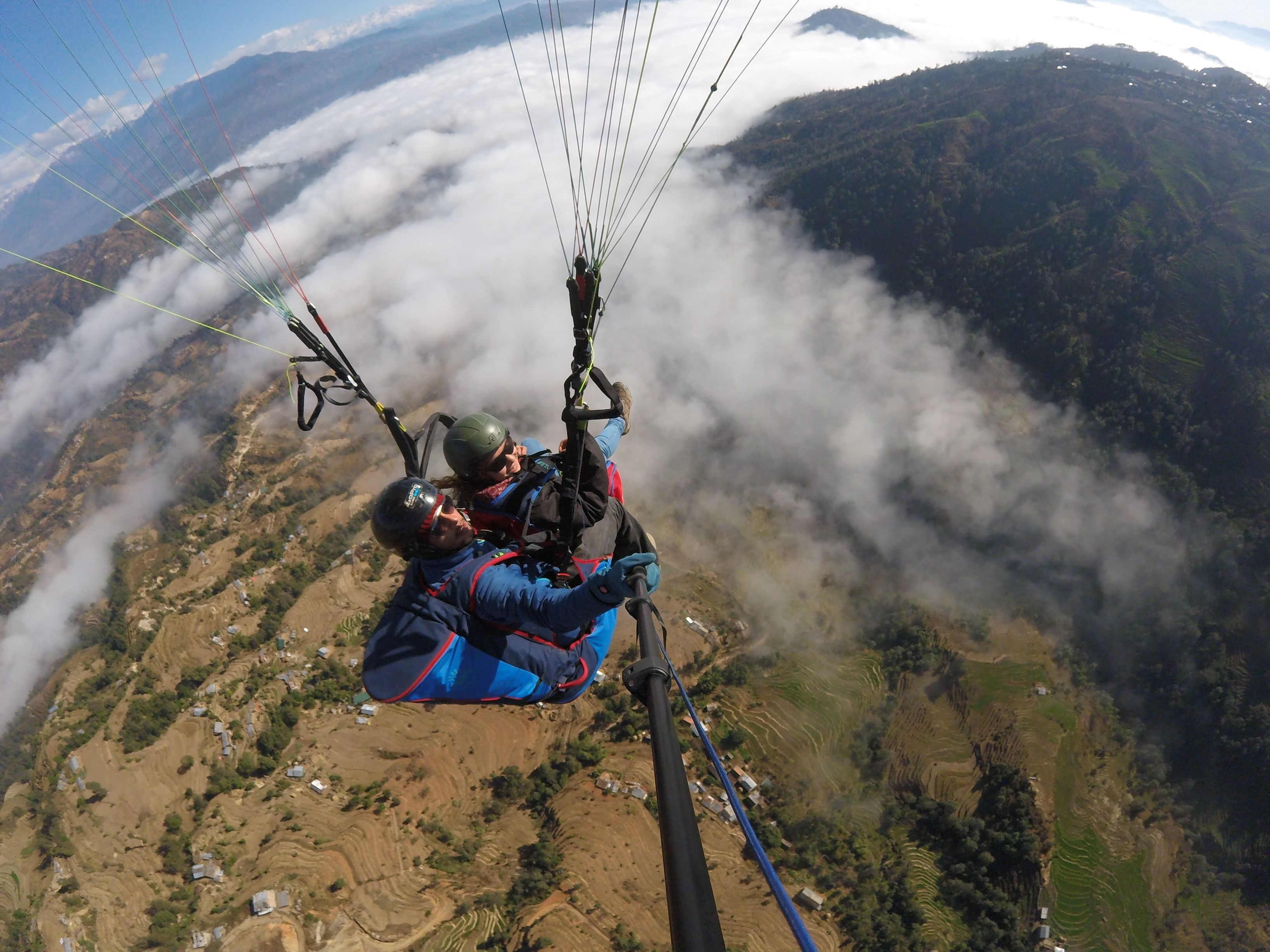 A person paragliding over a mountainous landscape with terraced fields below.