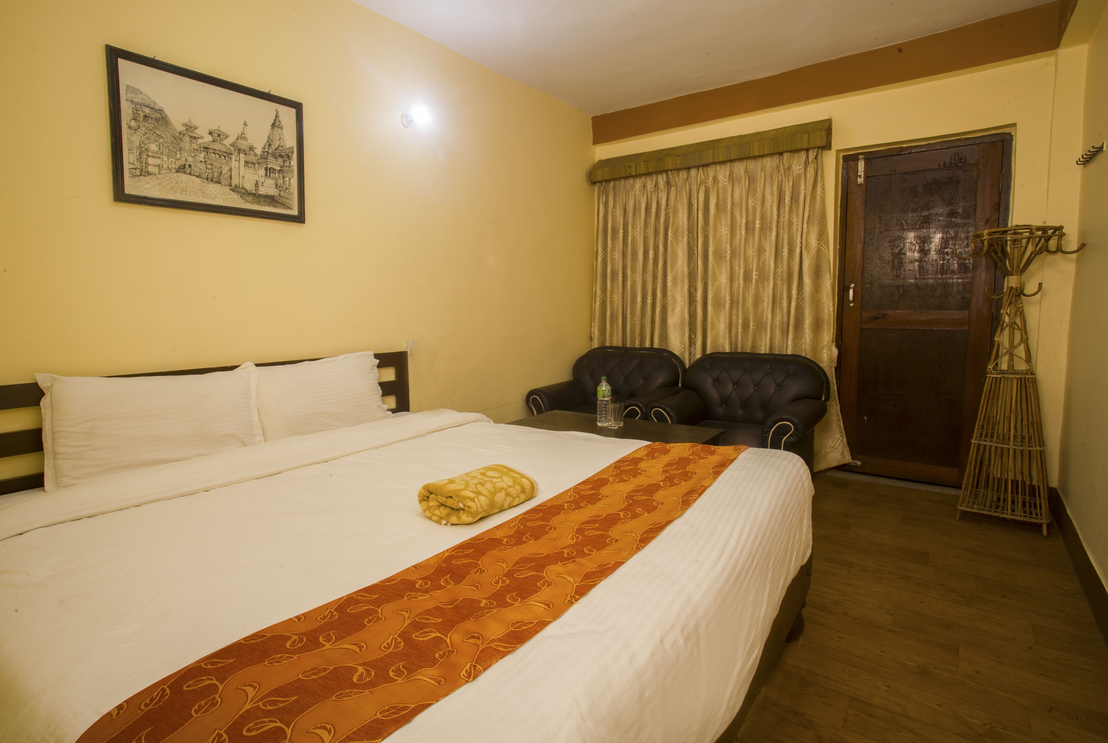 A neatly made bed with a patterned bedspread, a framed picture on the wall, a chair, and a door with a curtain.