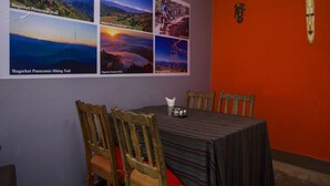 Een eetruimte met een tafel voor vier personen, houten stoelen en een muur versierd met zes ingelijste foto’s van landschappen.