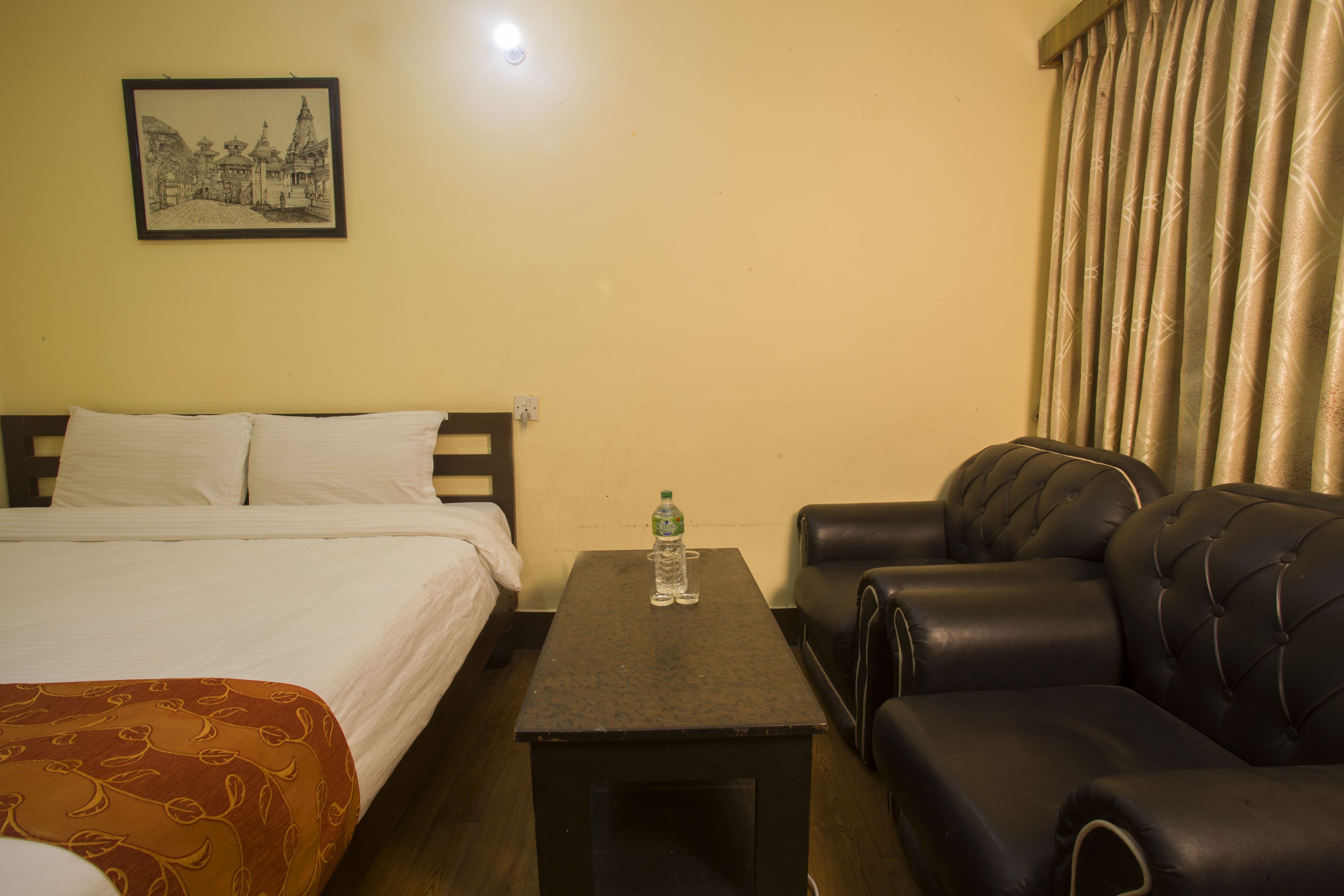 A hotel room with a bed, a small table with a bottle, and a leather sofa.