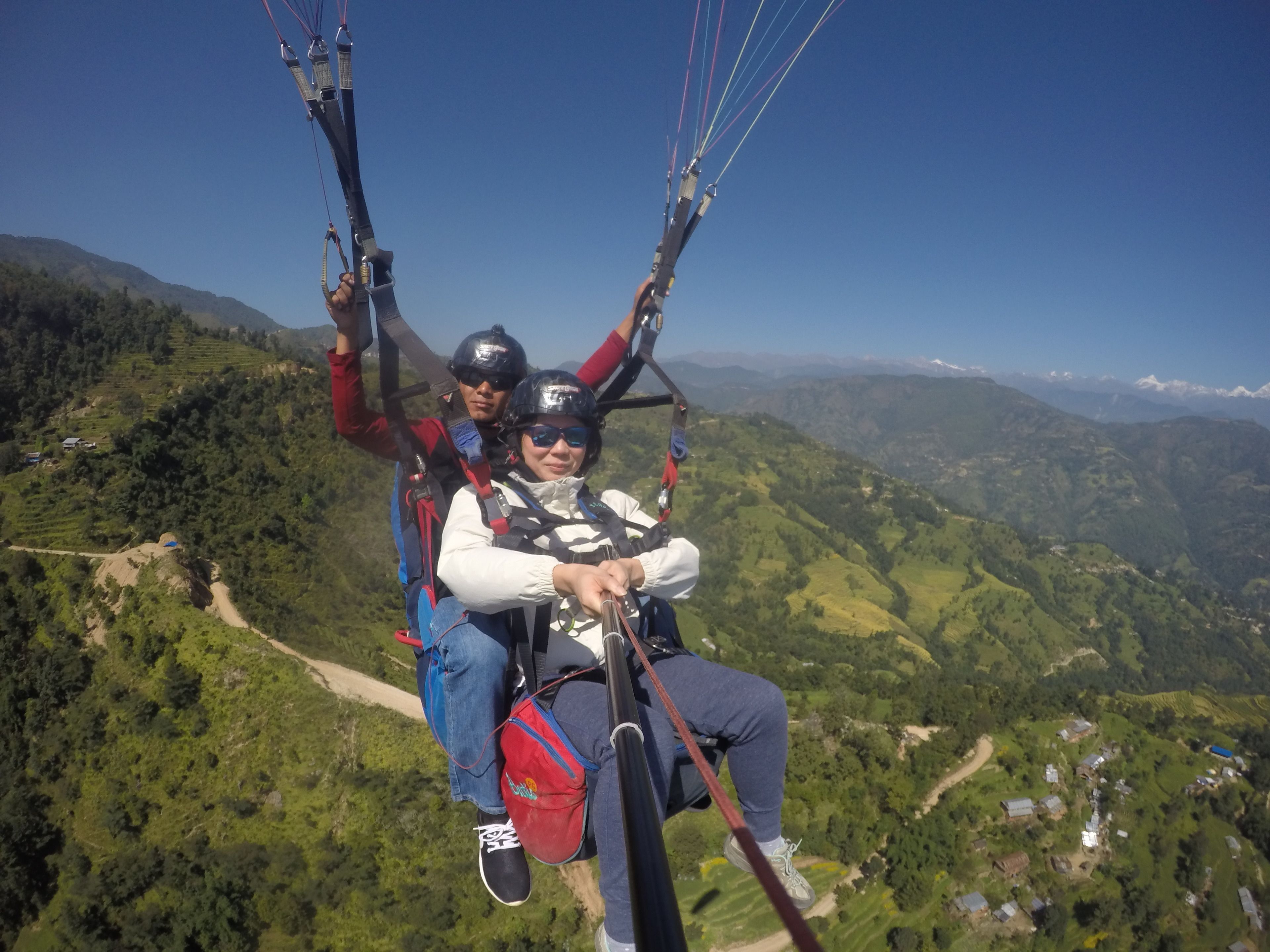 Una persona con arnés y paracaídas, suspendida en el aire con un paisaje montañoso debajo.