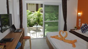 Ein Hotelzimmer mit Bett, Schreibtisch mit Laptop, Stuhl und Blick auf einen Garten durch eine Schiebetür.