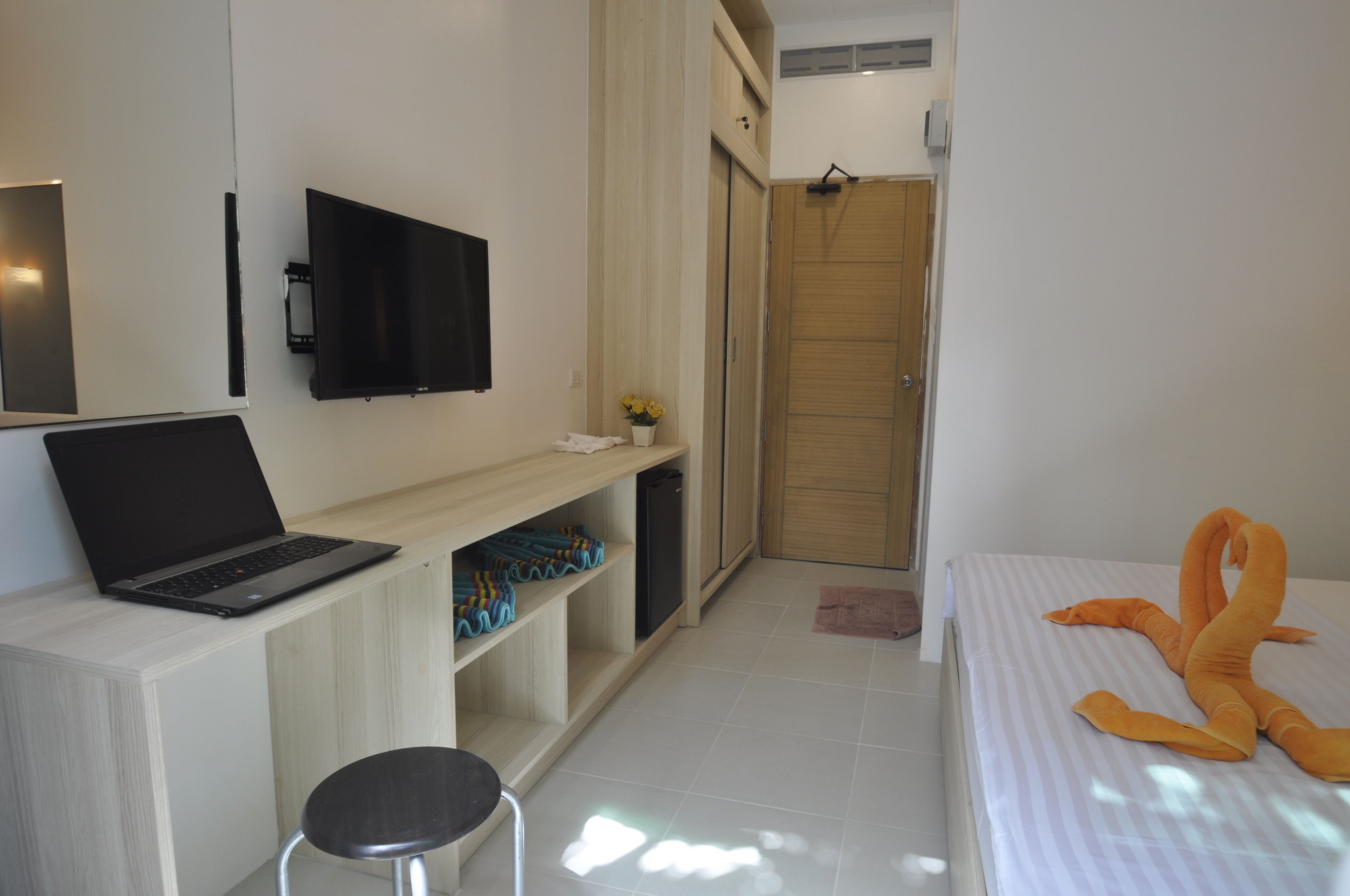 A modern hotel room with a flat-screen TV, a laptop on a desk, a bed with a striped blanket, and a wooden wardrobe.