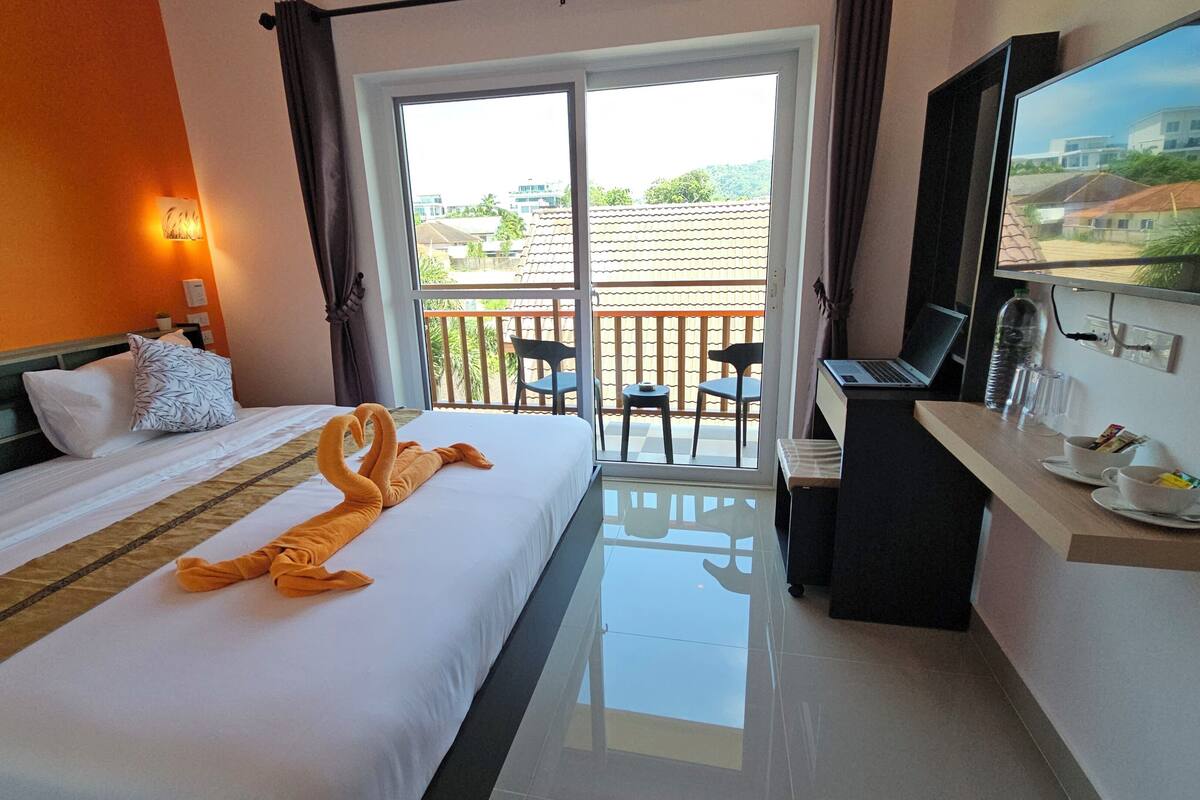 Habitación de hotel con una cama, un escritorio con una computadora portátil, un televisor y un balcón con sillas.