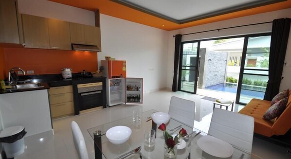 A modern kitchen with a dining area, a refrigerator, and a view of a swimming pool. - Duangjai Residence (Rawai)