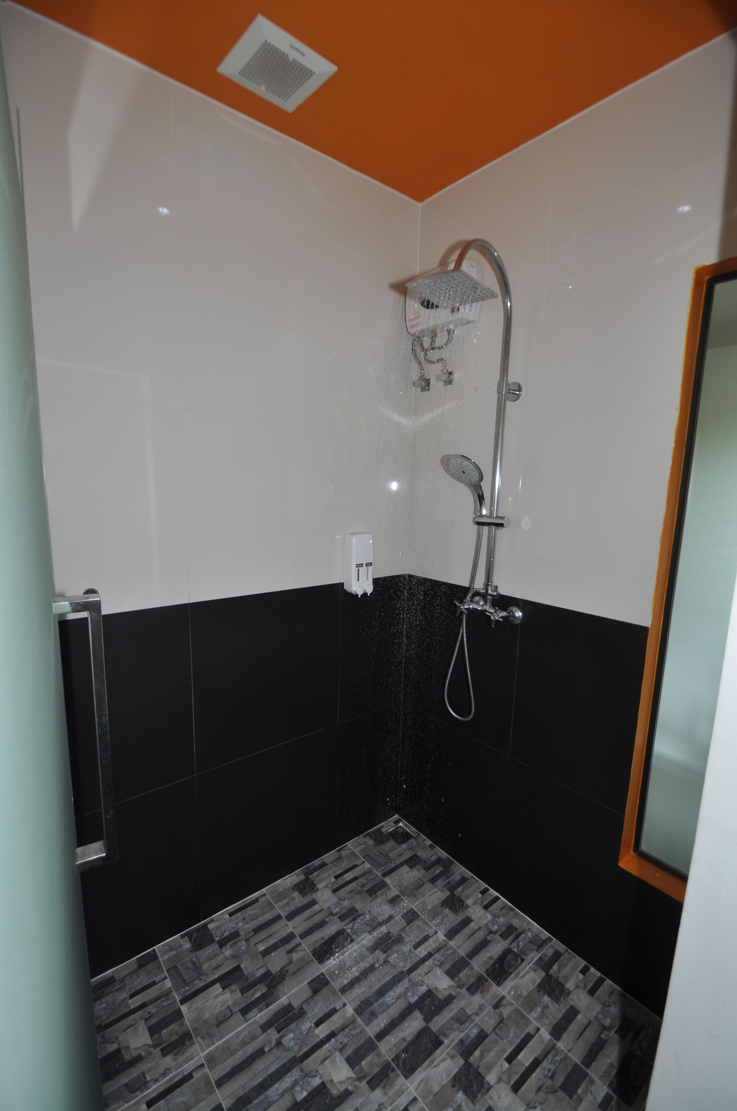 Un baño con ducha, paredes de azulejos blanco y negro, y un suelo con diseño.