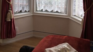 A corner room with a bay window, red curtains, and a bed with a white blanket. - Metro London City Airport (London)