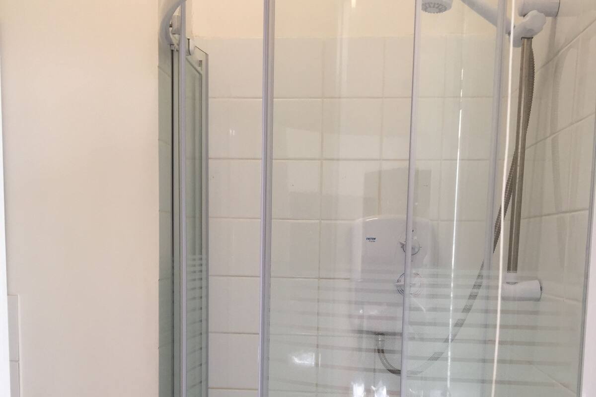 Een douchecabine van glas met een handdouche en een wandmengkraan.