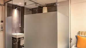 A modern hotel room with a glass partition separating the bathroom, a bed with an orange bedspread, and a small rug on the floor. - Vavien Hotel (Istanbul)