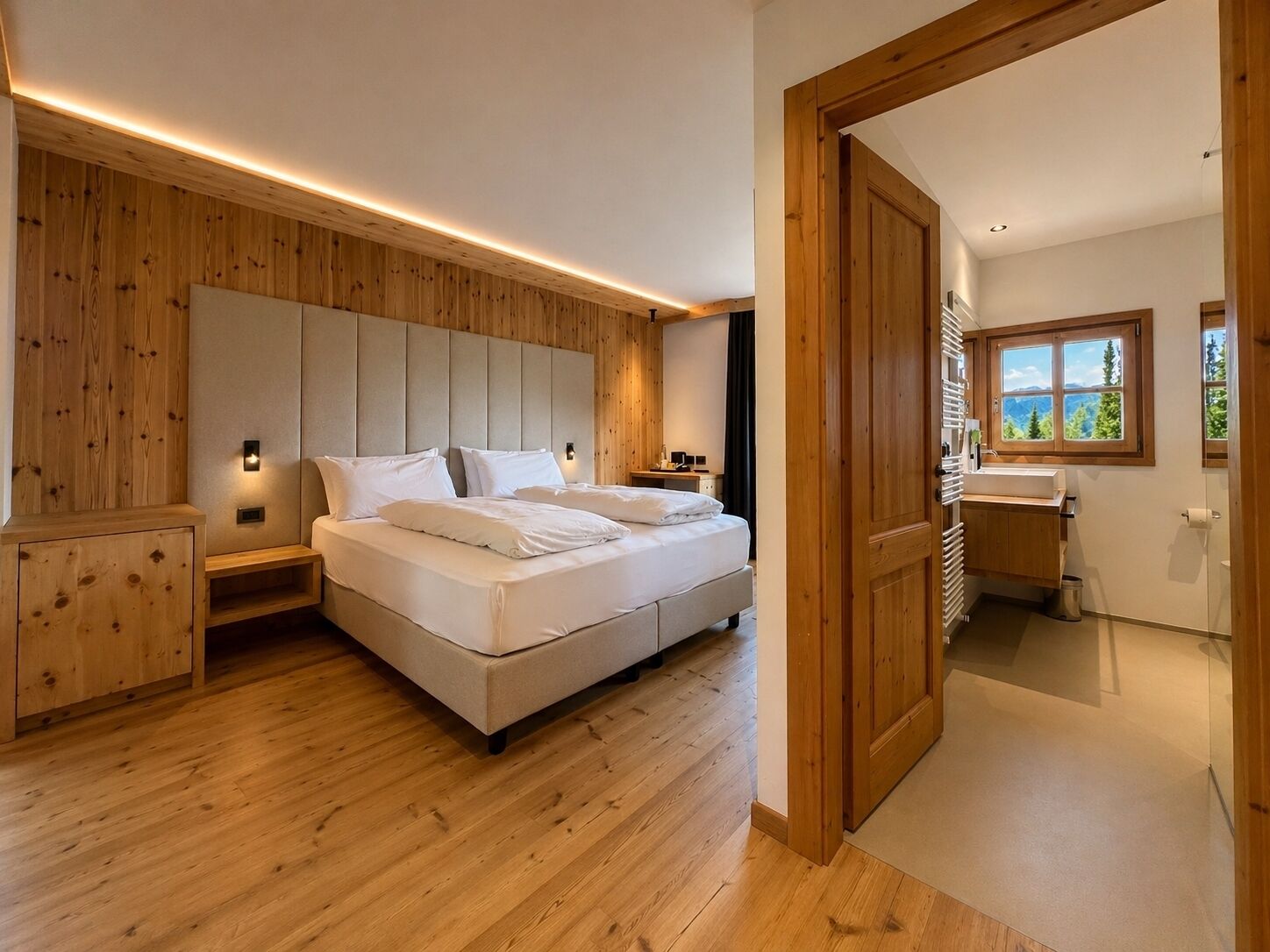 Ein Schlafzimmer mit Bett, Nachttischen, einem Holz-Kopfteil, einem Fenster und einem Badezimmer mit Waschbecken und Spiegel.