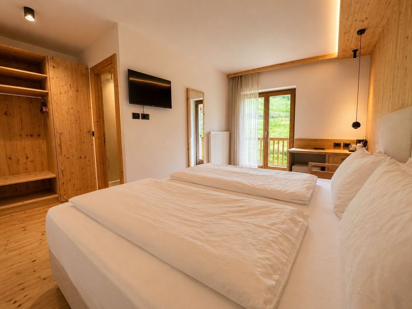 A bedroom with two beds, a TV, a wooden wardrobe, and a balcony with a view.