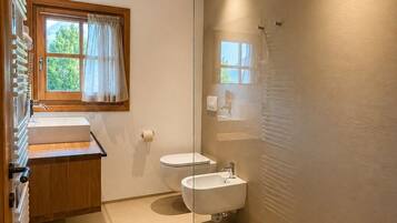 A modern bathroom with a glass shower enclosure, a wooden vanity, a toilet, and a bidet.