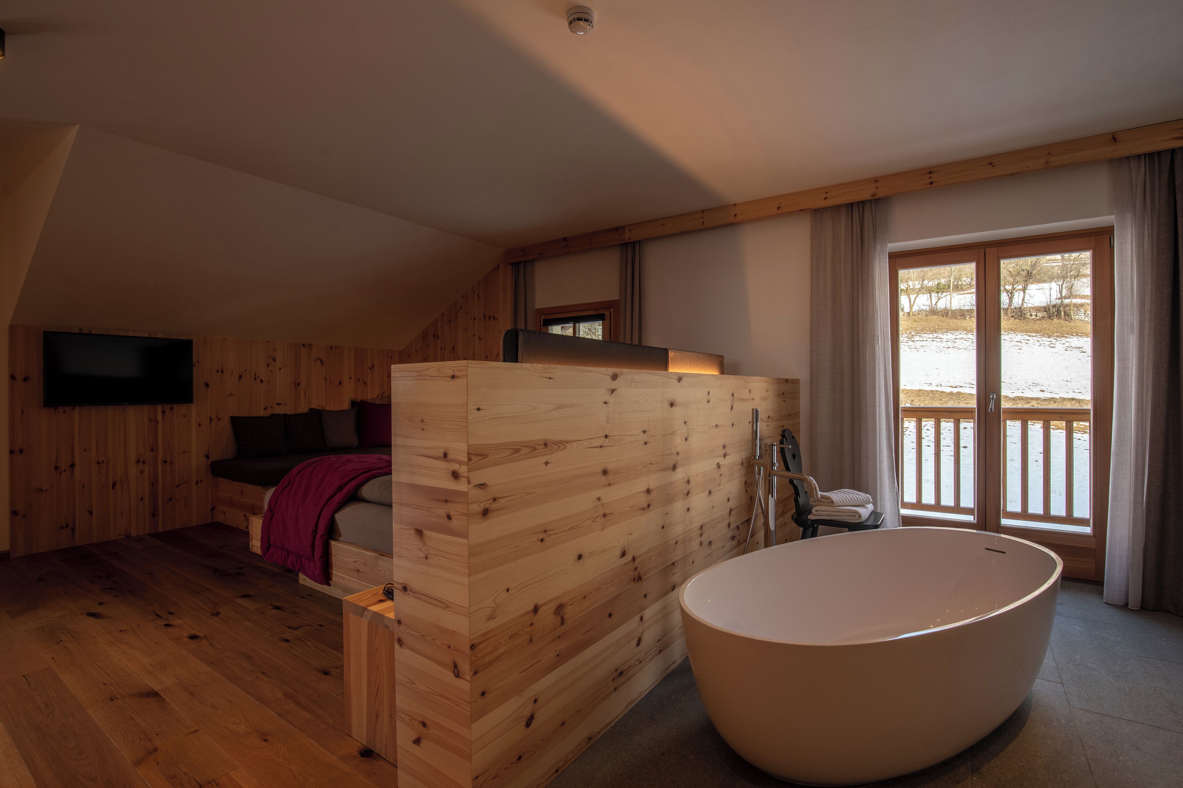 A wooden interior with a large bathtub, a bed, and a TV mounted on the wall.