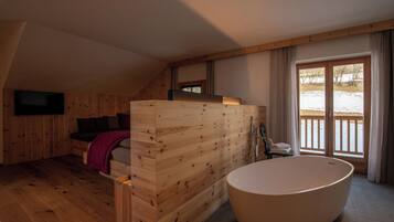 A wooden interior with a large bathtub, a bed, and a TV mounted on the wall.