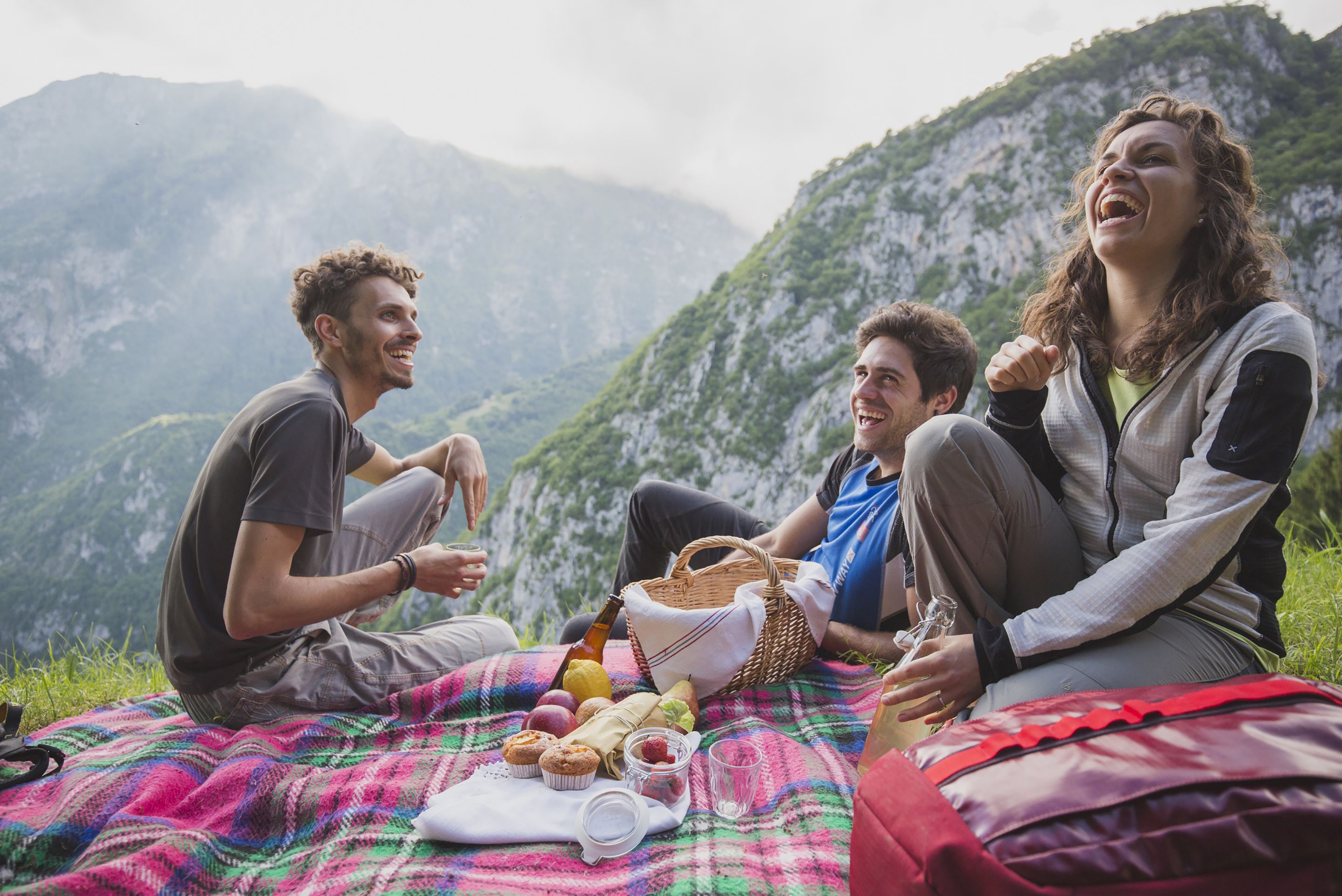 Un grupo de personas sentadas sobre una manta con una preparación para picnic en una zona montañosa.