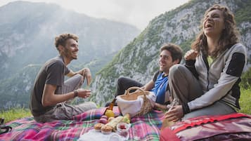 Un grupo de personas sentadas sobre una manta con una preparación para picnic en una zona montañosa.