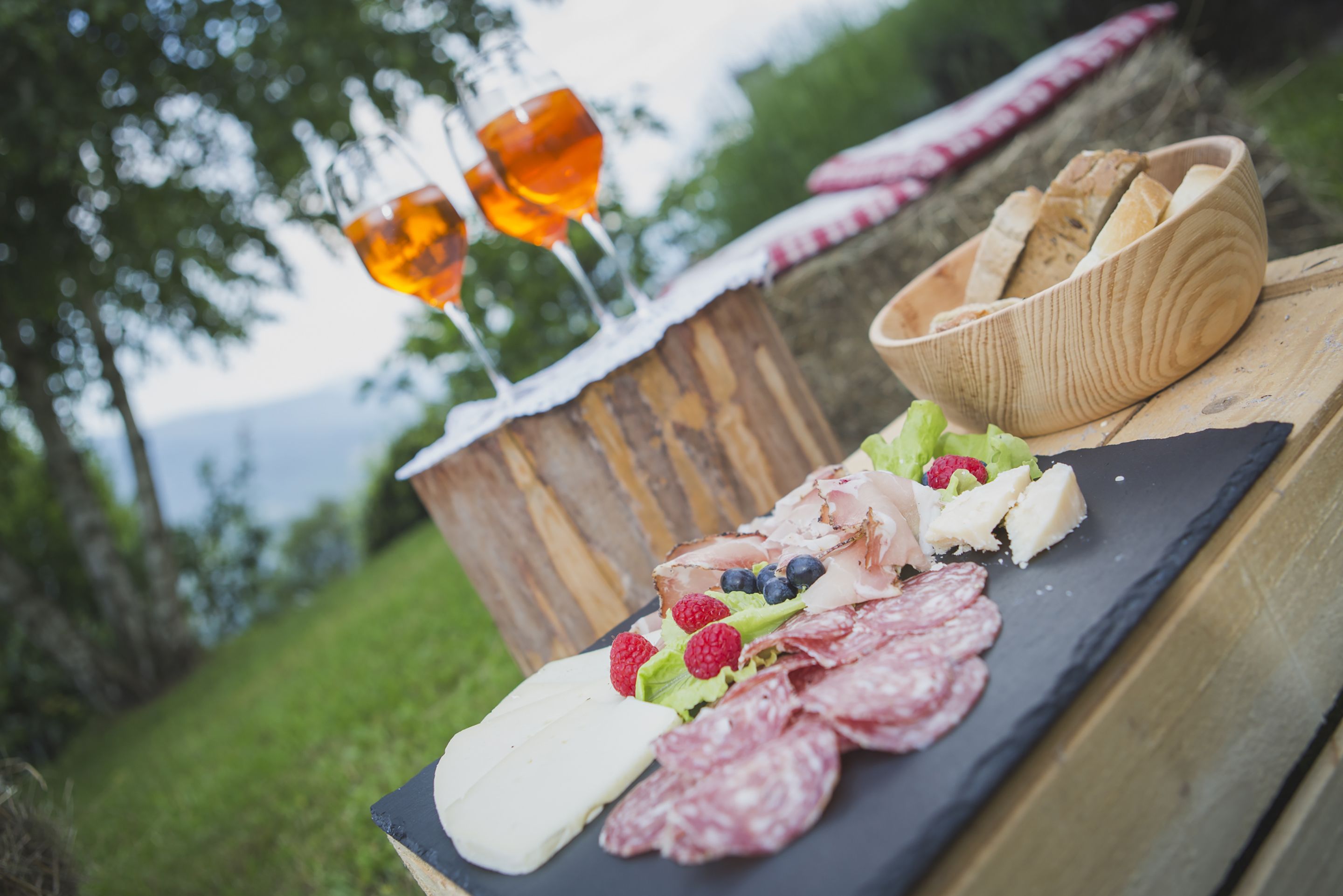 A wooden table with a charcuterie board, glasses of amber liquid, and a basket of bread.