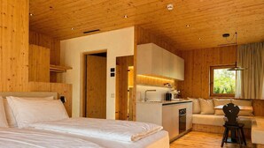 A wooden cabin interior with a large bed, kitchenette, and a sofa.