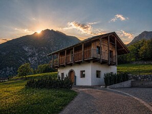 Um edifício em estilo chalé com varanda, ao pôr do sol, com montanhas ao fundo.