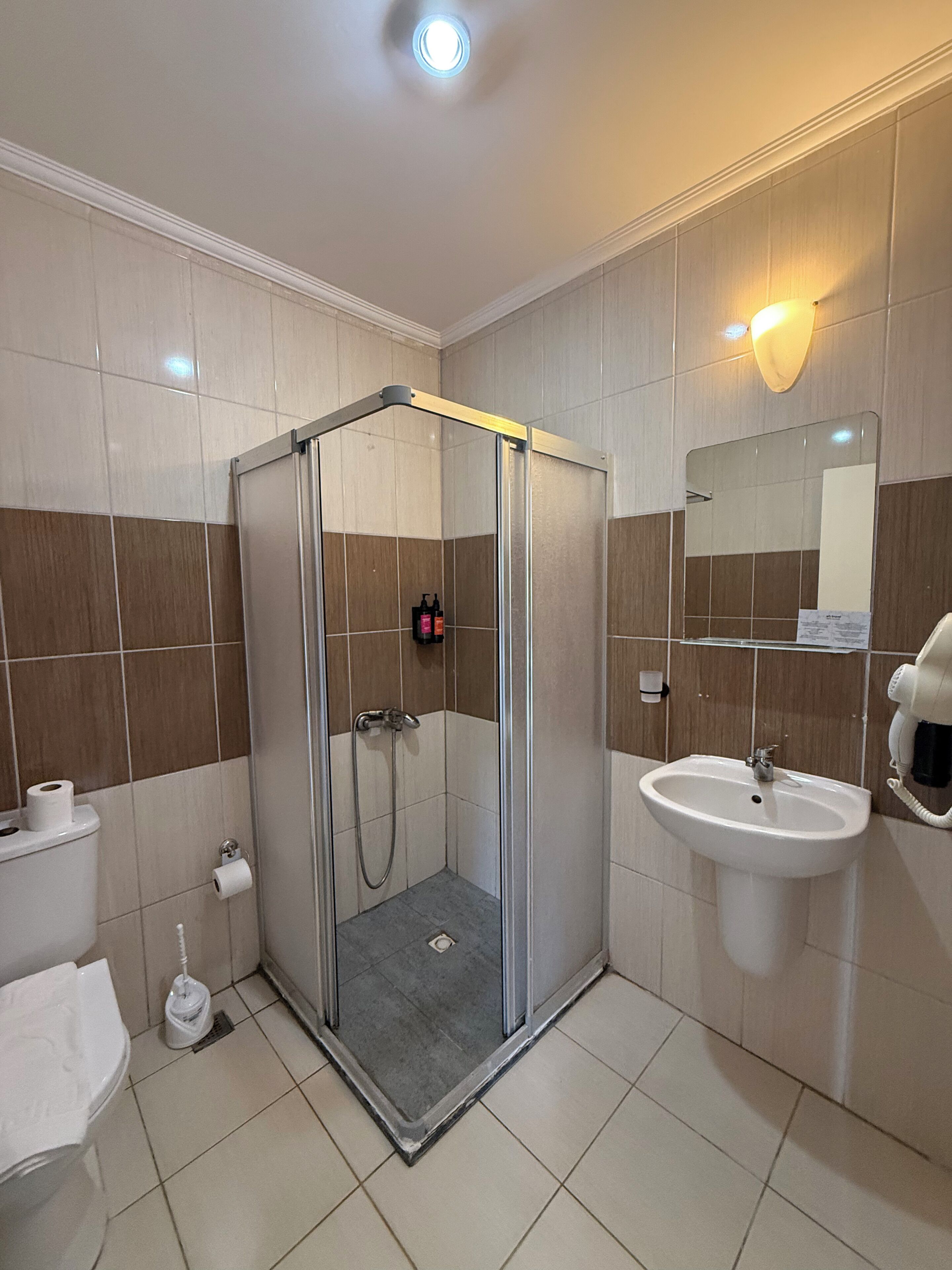 Een badkamer met een douchecabine van glas, een wastafel, toilet en een spiegel.