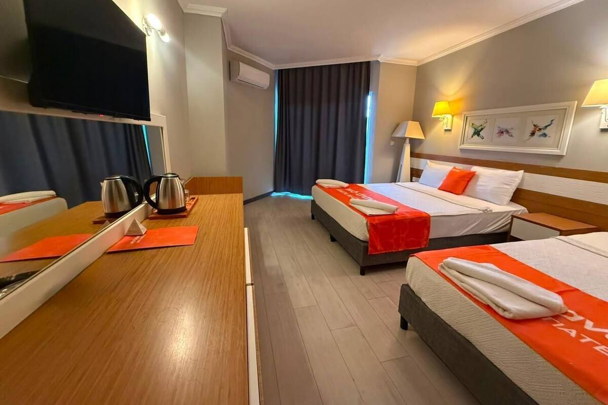 A hotel room with two beds, a wooden desk, a flat-screen TV, and a window with curtains.