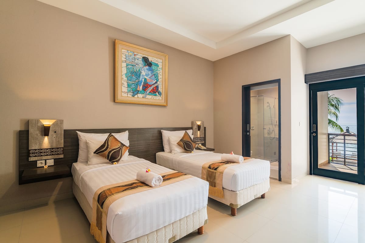 A hotel room with two beds, a painting on the wall, a shower area, and a balcony with a view.
