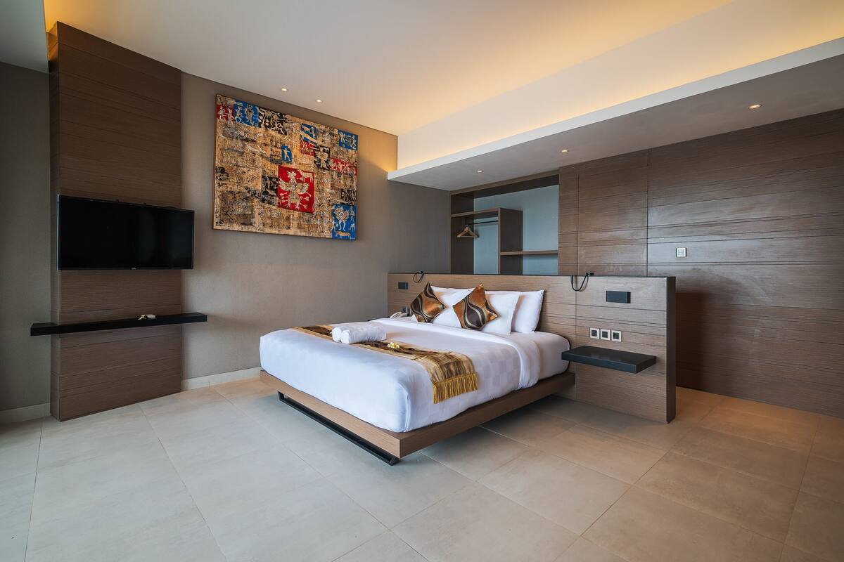 A modern bedroom with a large bed, a mounted TV, and a wall-mounted shelf.