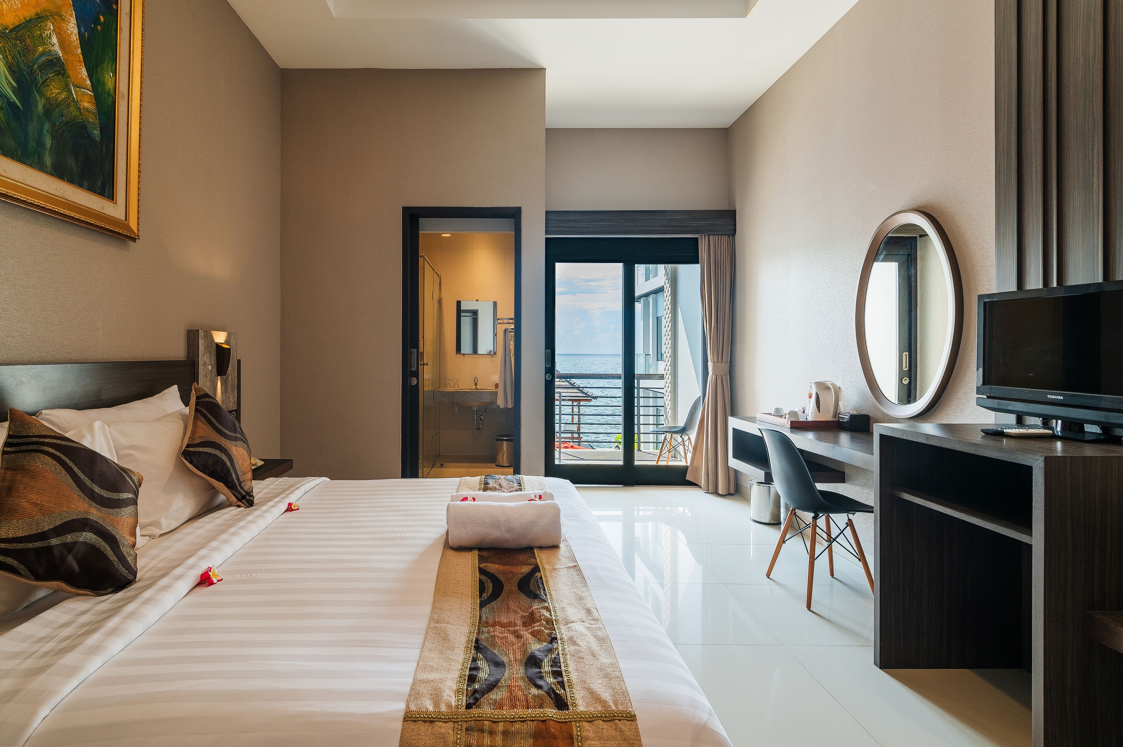 A hotel room with a bed, a desk, a TV, and a balcony with a view.