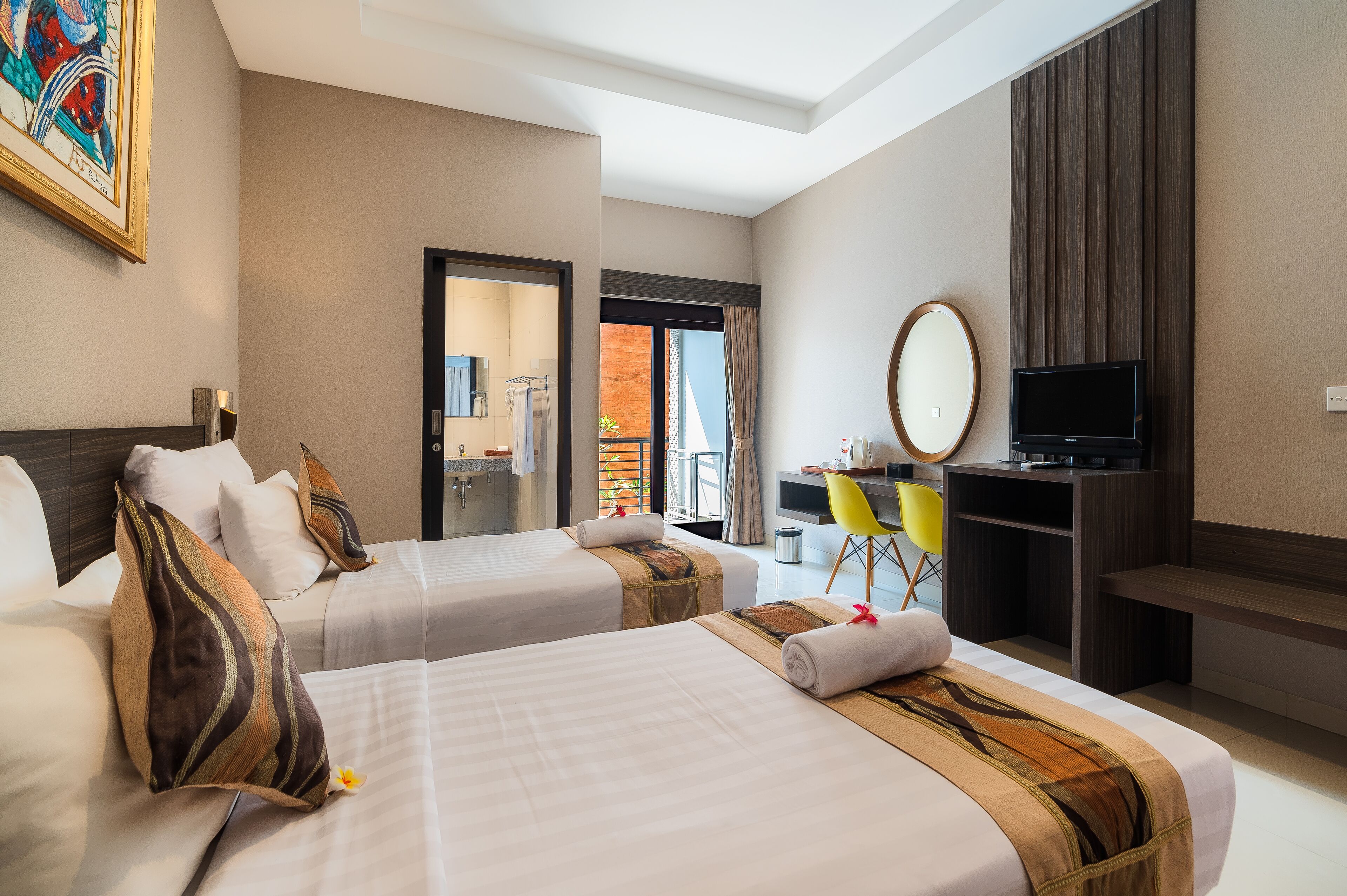 A hotel room with two beds, a desk, a TV, and a balcony with a view.