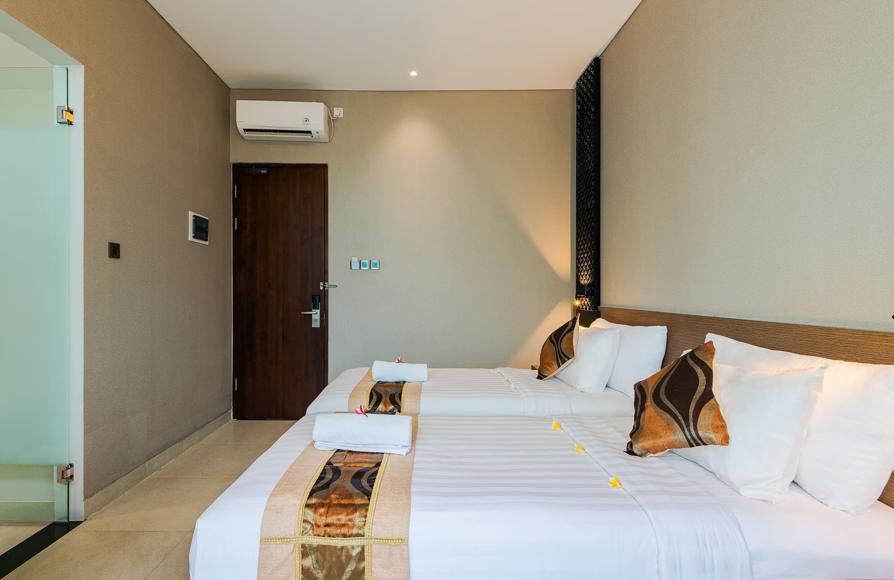 Een hotelkamer met twee bedden, een houten deur, een airconditioner en een klein raam.