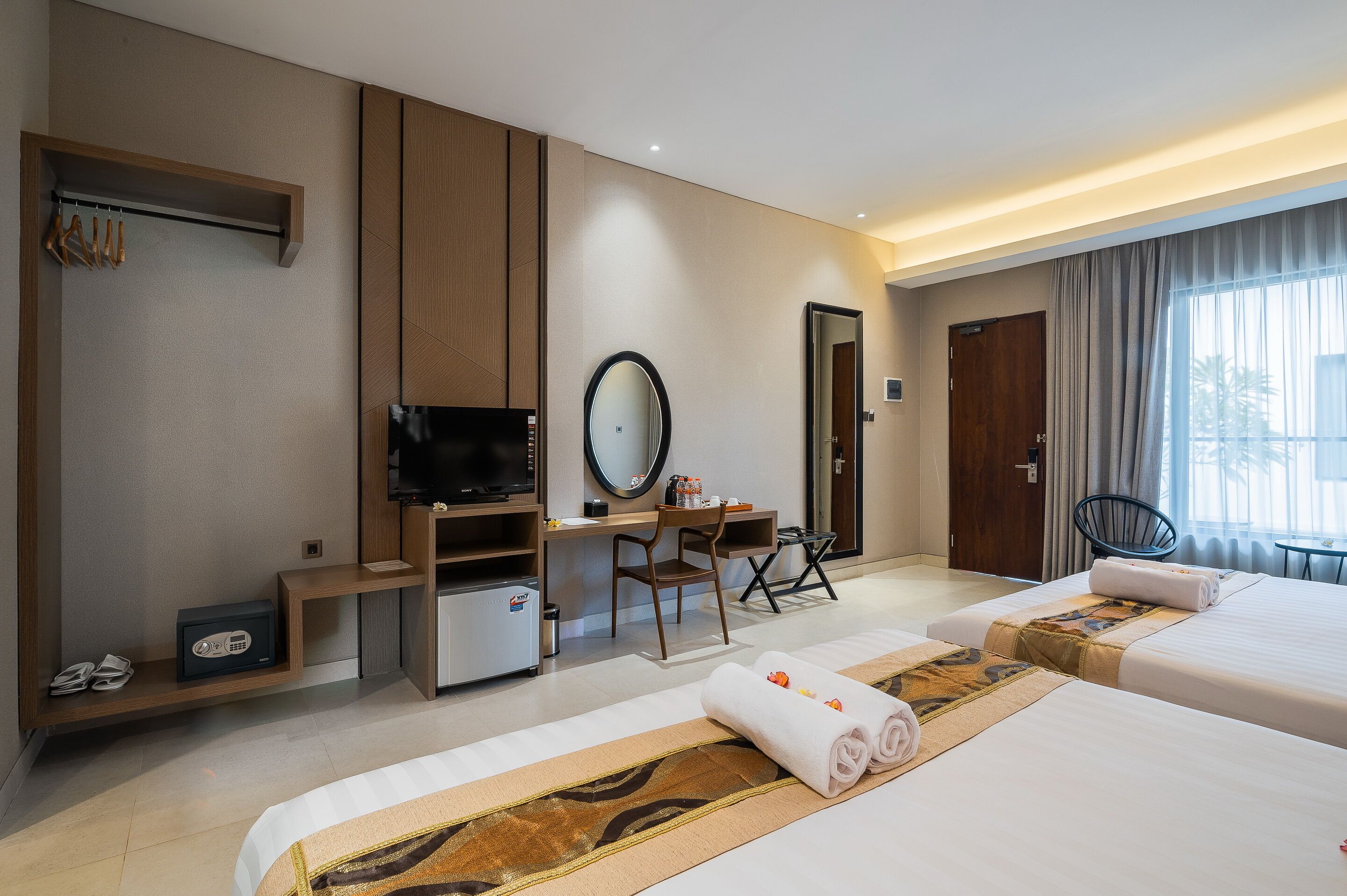 Una habitación de hotel con dos camas, un escritorio, un televisor, un espejo y un armario.