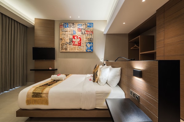Una habitación de hotel moderna con una cama grande, un televisor montado y un cabecero de madera.