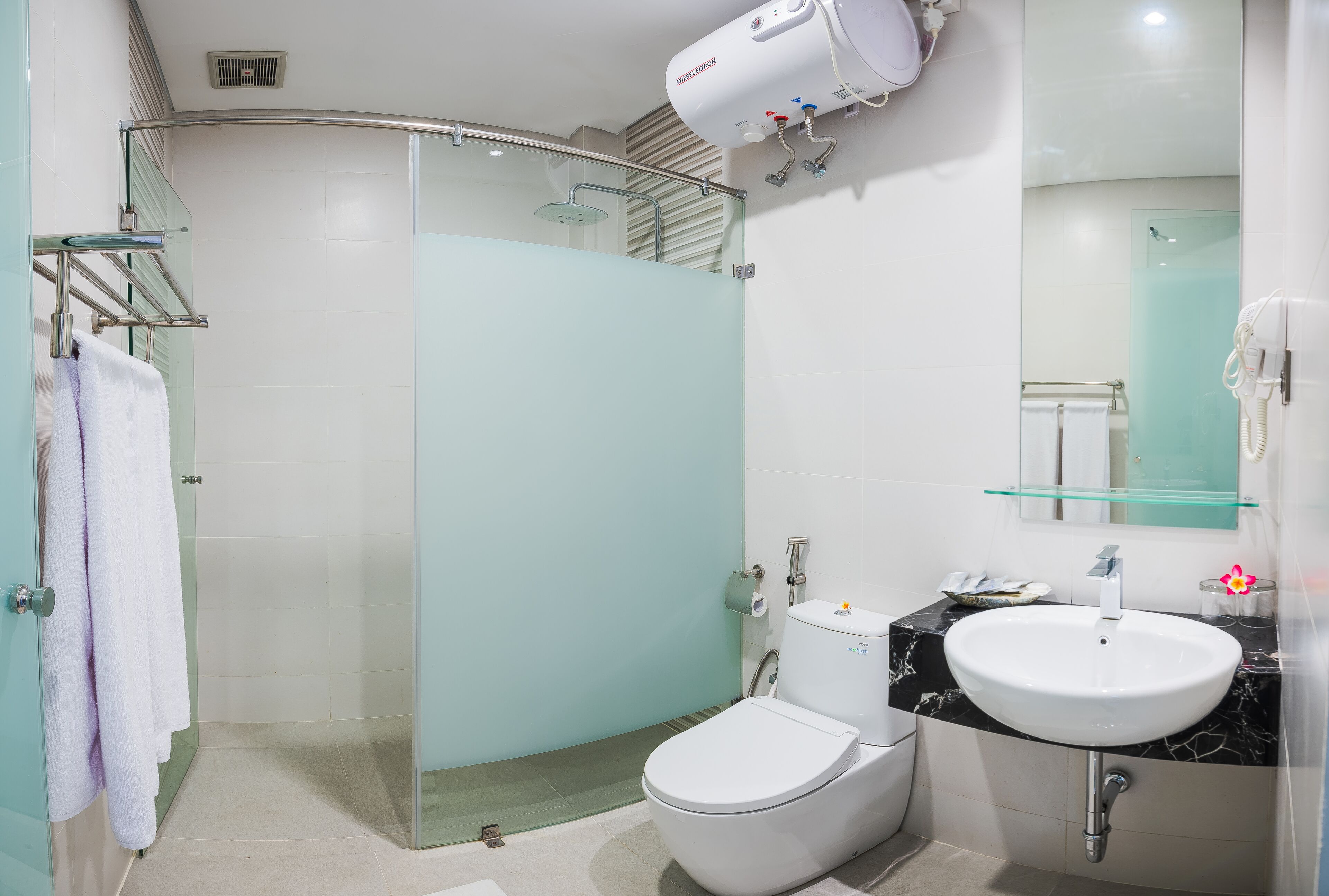 Un baño moderno con cabina de ducha de vidrio, inodoro blanco, lavamanos de mármol y estante de vidrio sobre el lavamanos.